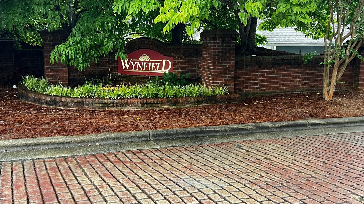 Brick entrance monument with the Wynfield name in gold lettering surrounded by landscaping and a brick paver drive